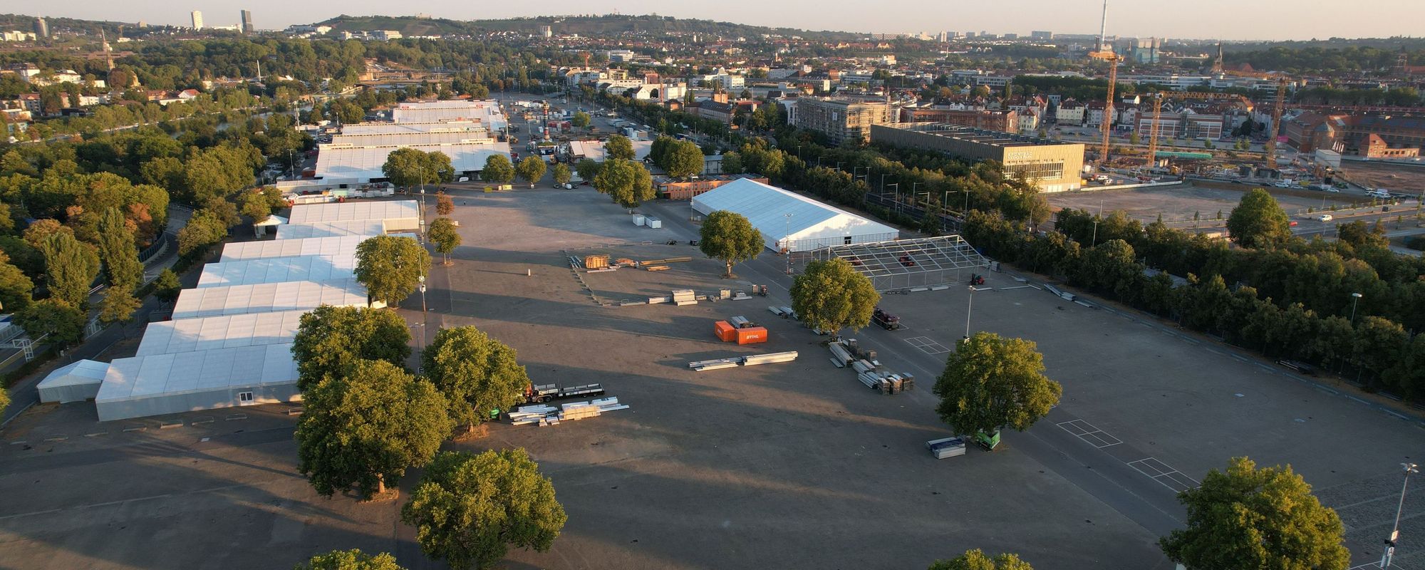 Vogelperspektive auf den Cannstatter Wasen bei Sonnenaufgang. Die Zelte eines Festes stehen aufgereiht.