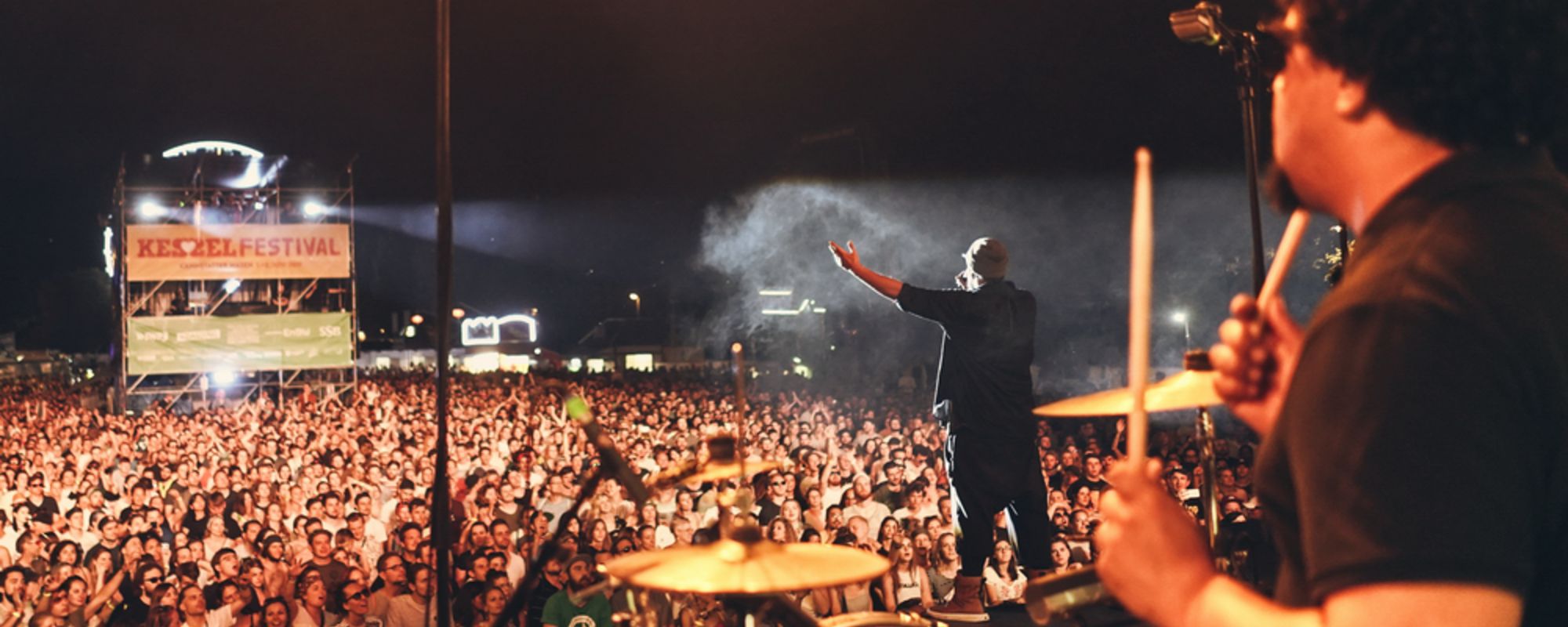 Blick über die Schulter eines Schlagzeugers von der Bühne auf dem Wasen auf das feiernde Publikum davor