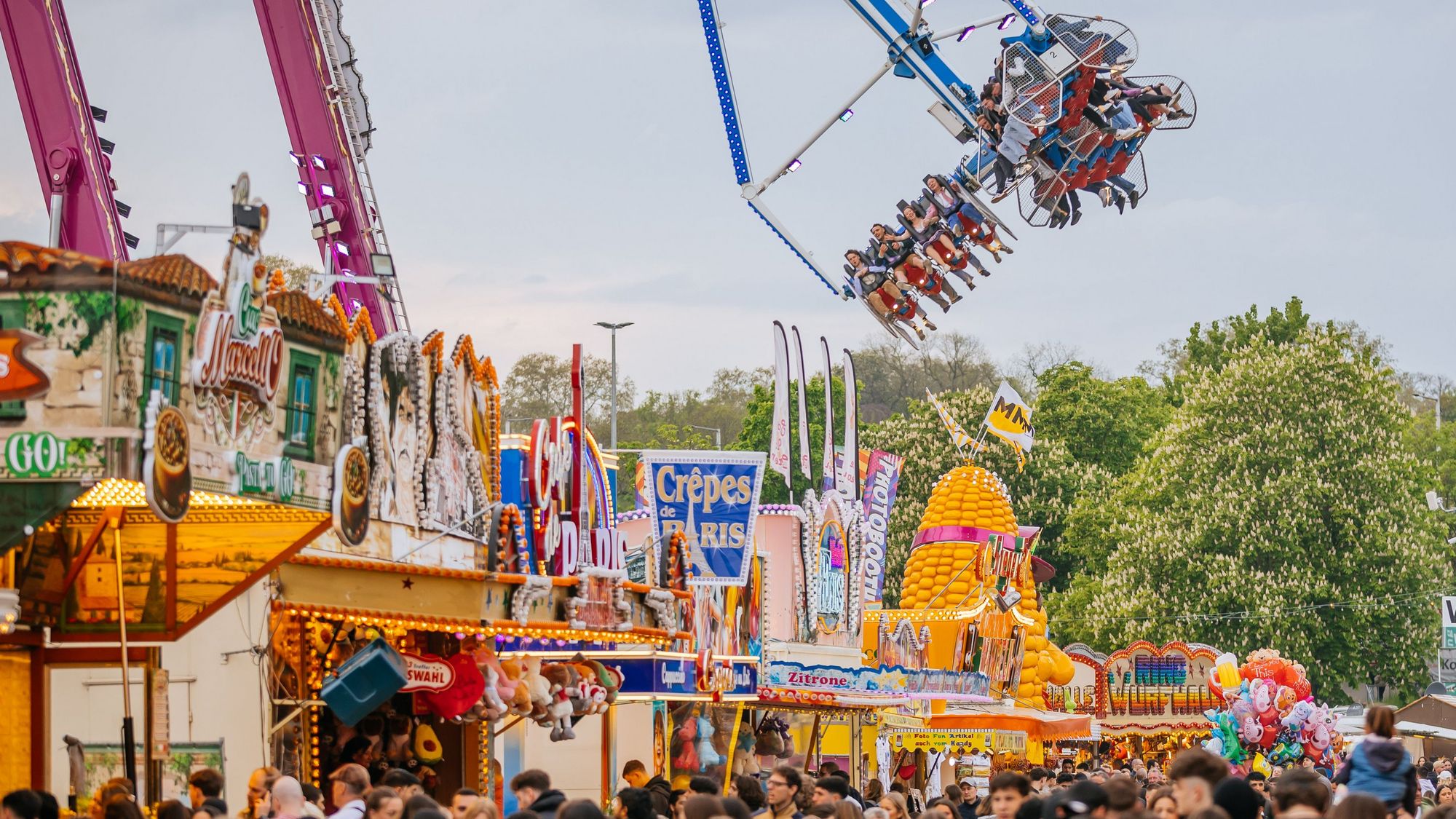 Menschen bahnen sich den Weg durch eine Gasse des Frühlingsfestes. Über ihnen dreht ein Fahrgeschäft seine Bahnen mit Fahrgästen