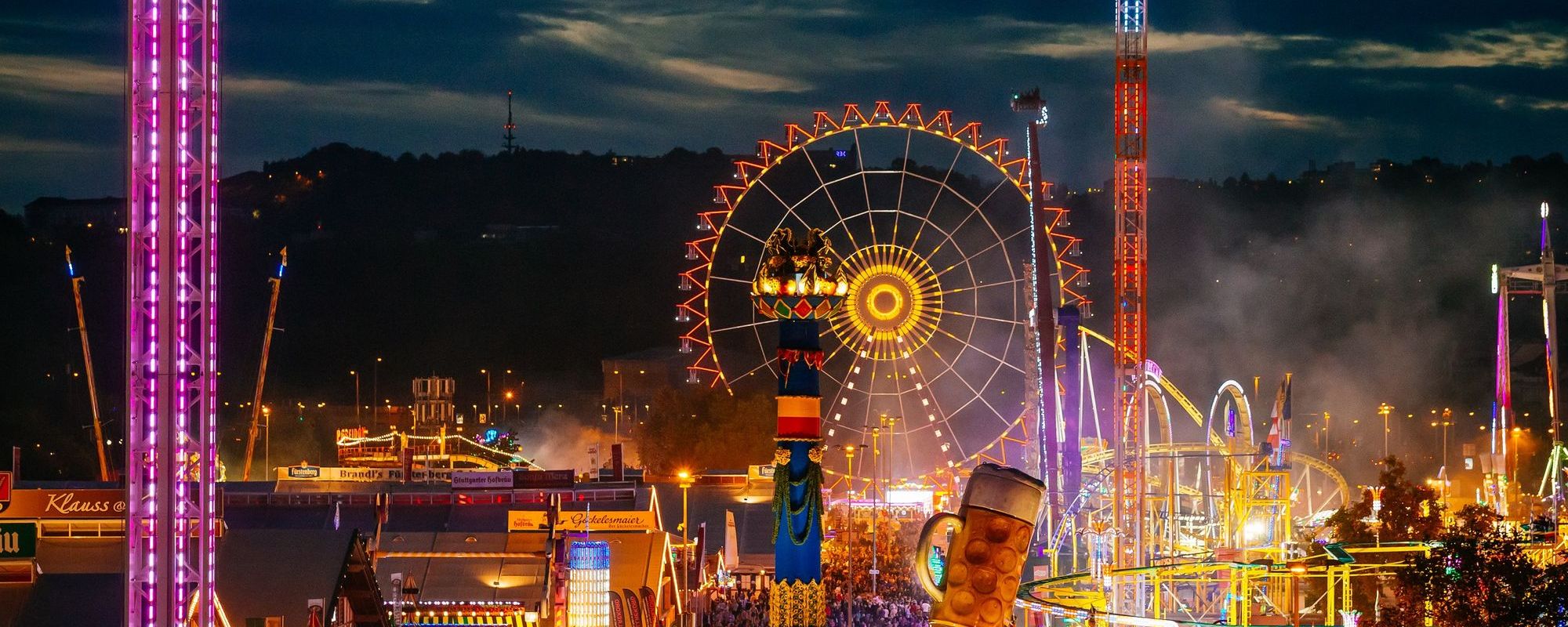 Blick auf das Cannstatter Volksfest aus der Vogelperspektive bei Dämmerung mit Freefall-Tower, riesenrad, Achterbahn, Infinity-Fahrgeschäft und schönen Lichtern